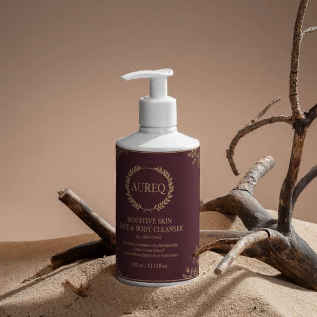 Sensitive Skin Face & Body Cleanser in a pump bottle on sand with natural elements.