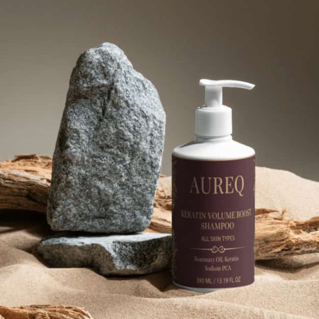 AUREQ Keratin Volume Boost Shampoo bottle on sandy surface with rocks, promoting volume and strength for flat hair.