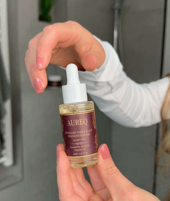 Hand holding a bottle of Aureq hair care product with a dropper.