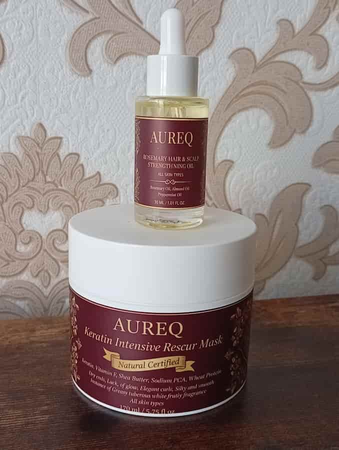 Aureq hair care products including a mask and serum on a wooden surface with a decorative wall background.
