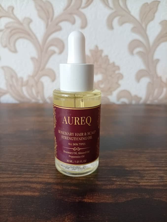 Aureq hair and scalp oil bottle on a wooden surface with a decorative wall background