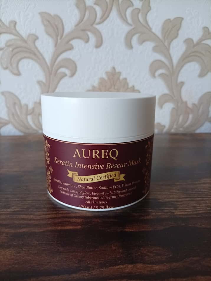Aureq Keratin Intensive Rescue Mask jar on a wooden surface with decorative wall paper in the background
