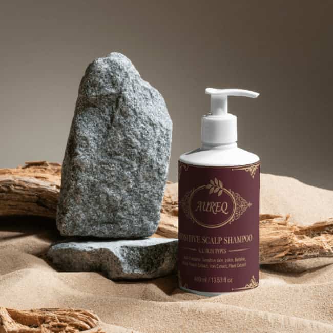 Sensitive Scalp Shampoo bottle next to a rock on sand background, highlighting gentle hair care for sensitive scalps.