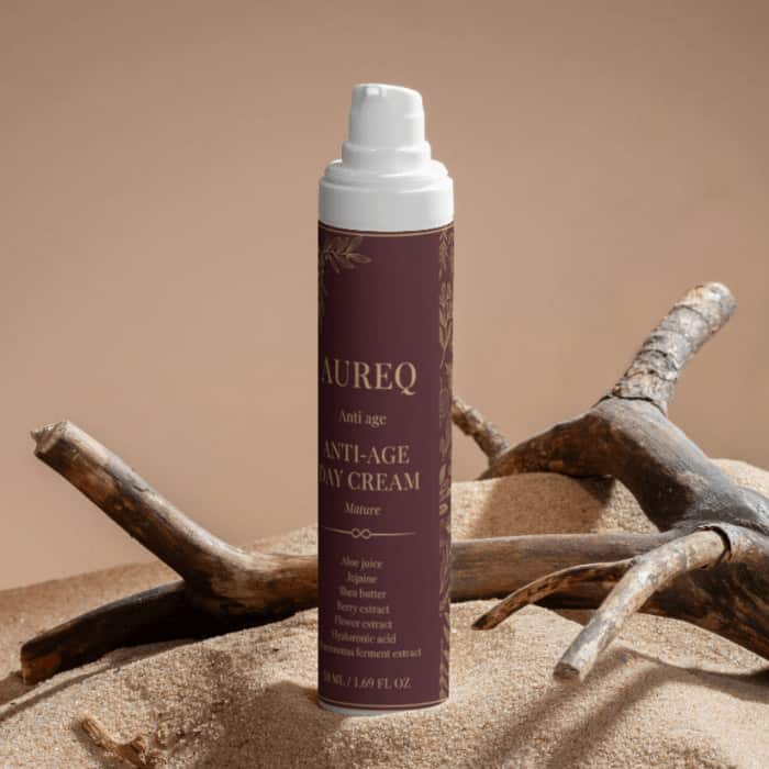 Aureq Anti-Age Day Cream bottle on sandy surface, promoting hydration and skin firmness.