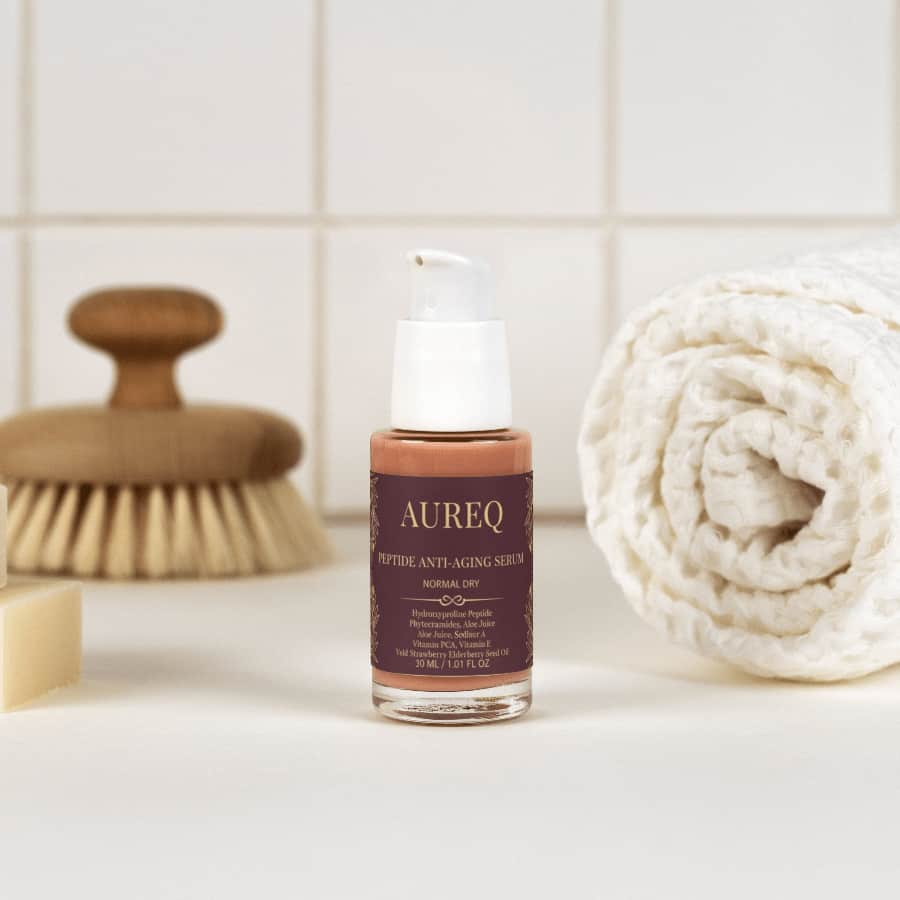 AUREQ Peptide Anti-Aging Serum bottle on a bathroom countertop with a brush and towel.