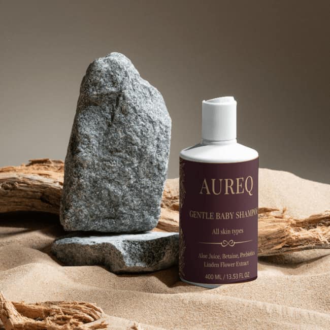 AUREQ Gentle Baby Shampoo - Nurturing Care for Delicate Scalps beside a rock, showcasing its gentle formula.