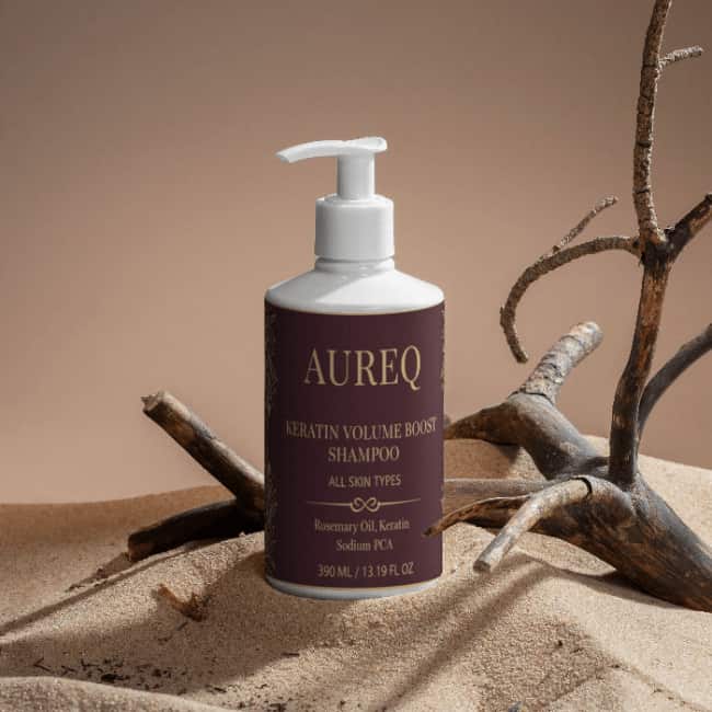 AUREQ Keratin Volume Boost Shampoo bottle on a sandy surface, designed for all skin types.