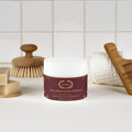 Deep Cleanse Scalp Scrub, Rosemary & Mint on a bathroom counter surrounded by hair care items.